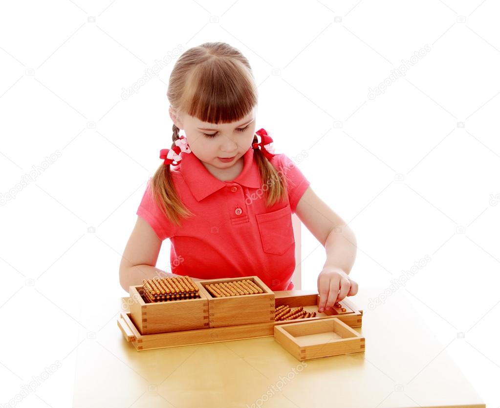 Adorable little blonde girl sitting at table and studying math in a Montessori kindergarten, close-up