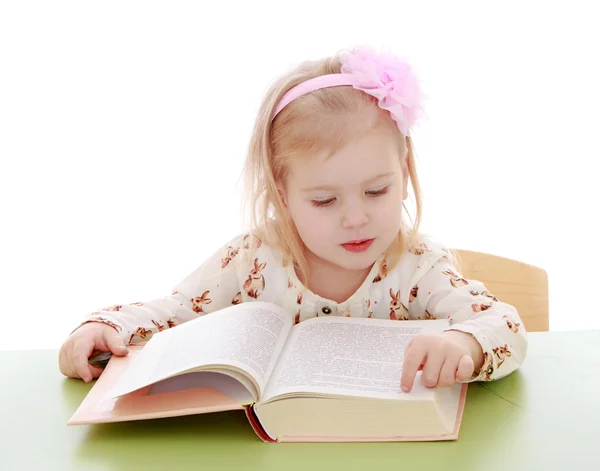 Little Caucasian blond girl sitting at a Desk and read by syllables thick academic book — Stockfoto