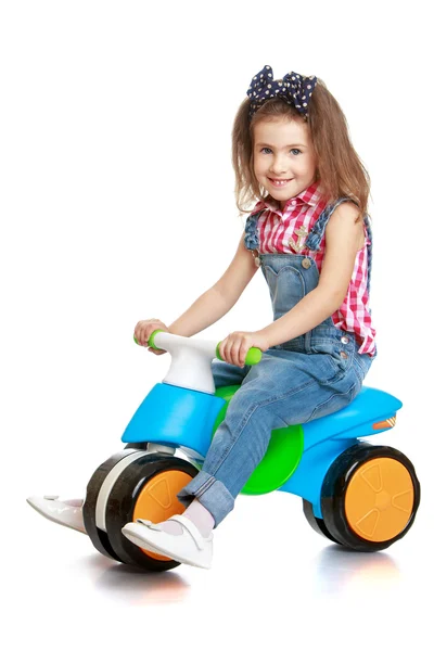 Funny little girl in denim overalls with straps riding a plastic bike — Stockfoto