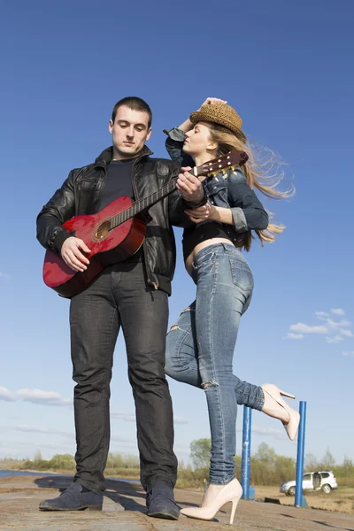 Giovane uomo che suona la chitarra acustica e sorridente donna tenendo il cappello — Foto Stock