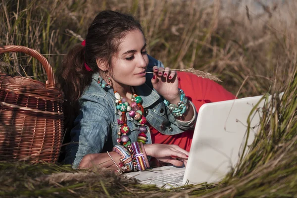 Ragazza dai capelli lunghi sdraiata al computer portatile e con in mano un'erba — Foto Stock