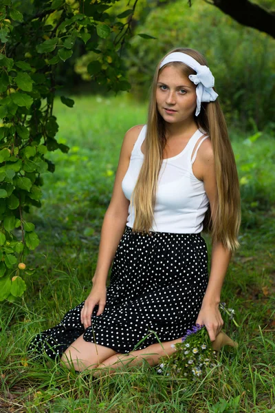 Hermosa chica con flores sentadas de rodillas en el jardín verde —  Fotos de Stock