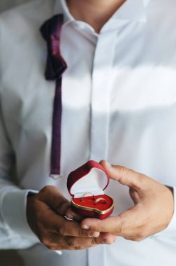 Bir çift altın alyans kırmızı kalp şeklinde bir kutuda. Düğün gününde damat ellerinde.