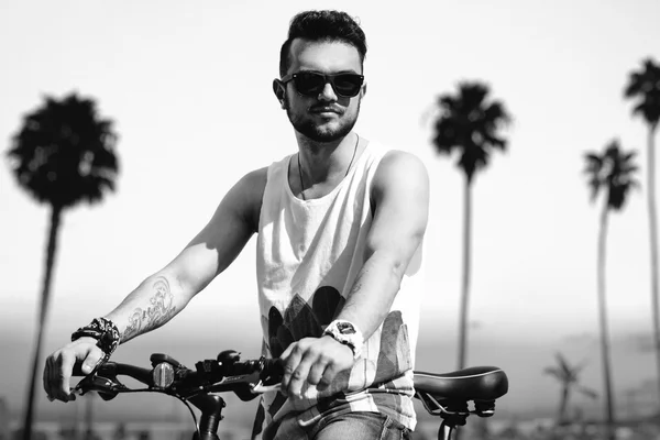 Joven hombre hipster en la playa en el soleado día de verano con bicicleta —  Fotos de Stock