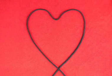 Kırmızı arkaplanda kalp şeklinde siyah ip.