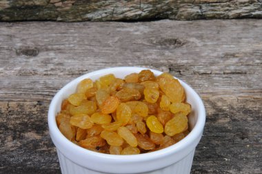 Beyaz bir kasede kuru üzümler ahşap arka planda, üst manzara.