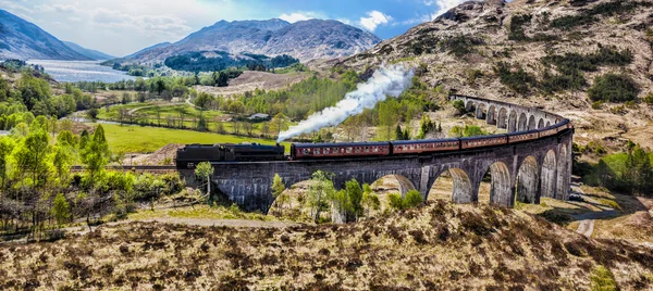 Glenfinnan Viaduto ferroviário na Escócia com o trem a vapor jacobita contra o pôr do sol sobre o lago — Fotografia de Stock