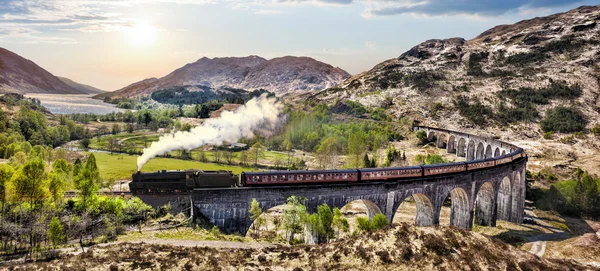 Glenfinnan Viaduto ferroviário na Escócia com o trem a vapor jacobita contra o pôr do sol sobre o lago — Fotografia de Stock