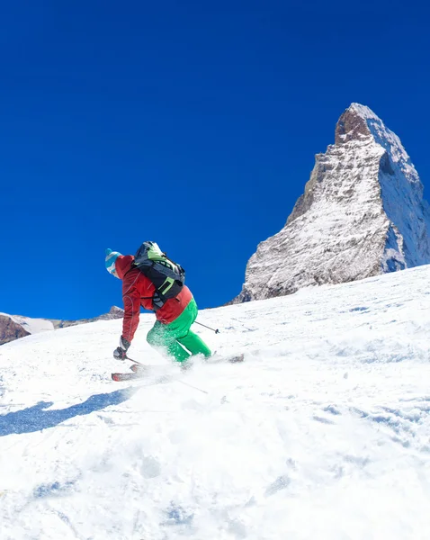 Skidåkare skidor utförsåkning i höga berg mot solsken — Stockfoto