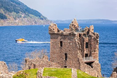 İskoçya 'daki Loch Ness Gölü' ndeki tekneye karşı Urquhart Kalesi harabeleri