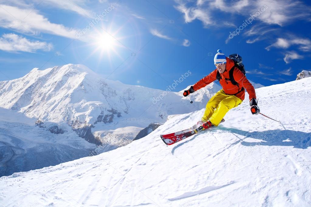 Skier skiing downhill in high mountains against blue sky