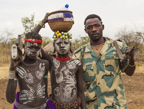 Boys from Mursi tribe and a solder with machine guns in Mirobey. Omo Valley. Ethiopia. — Stock Photo, Image