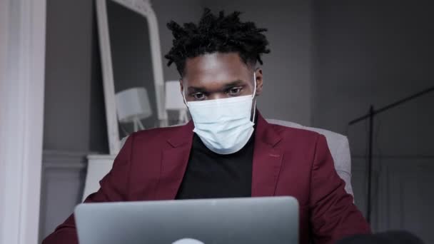 Un hombre negro trabaja en un primer plano portátil de su cara. video conferencias hombre usando máscara médica — Vídeos de Stock