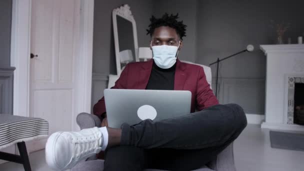 Zwarte zakenman werkt achter een laptop met een beschermend masker. Online conferentie — Stockvideo