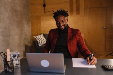 Odaklanmış Afrikalı genç işadamı kulaklık takıyor internetten internetten internetten internetten internetten internet yayınları izliyor eğitim dersleri konferansını dinliyor notlar alıyor çalışma masasında oturuyor, konsept öğreniyor.