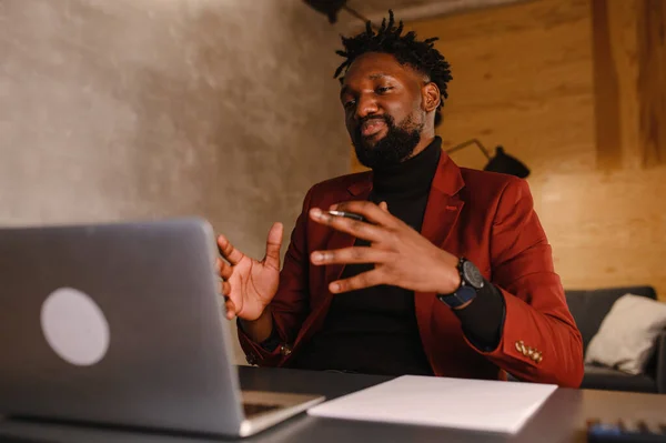 自信を持って若いアフリカ人男性はオフィスでウェブカメラ会議ビデオ通話を見て、幸せな混合レース起業家はオンラインビデオチャットジョブインタビューを行う話は机の上に座る — ストック写真
