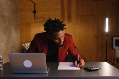  Siyah iş adamı hesap makinesine güvenir ve notlar alır. Finansör ya da muhasebeci evden çalışır