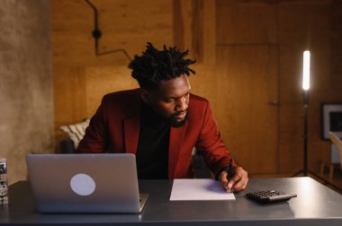  Siyah iş adamı hesap makinesine güvenir ve notlar alır. Finansör ya da muhasebeci evden çalışır