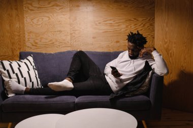  Siyah adam kanepede dinleniyor ve telefona bakıyor.