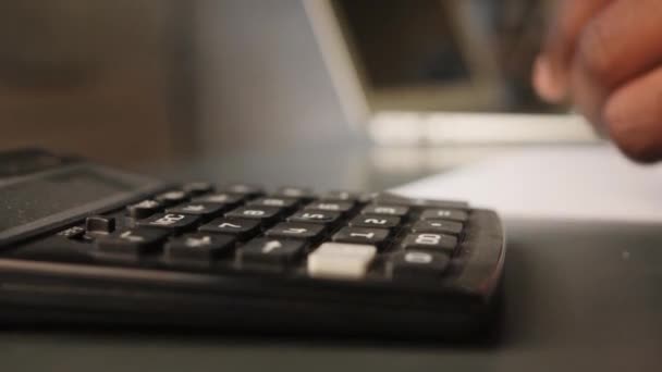 Черный бизнесмен рассчитывает на калькулятор и делает заметки. финансист или бухгалтер работает на дому — стоковое видео