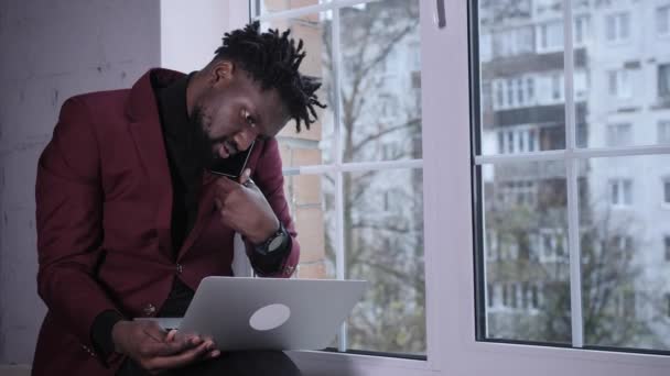 Souriant beau jeune homme afro-américain assis, regardant l'écran d'ordinateur. Homme biracial millénaire concentré travaillant sur un projet dans un bureau moderne ou étudiant en ligne à la maison. — Video