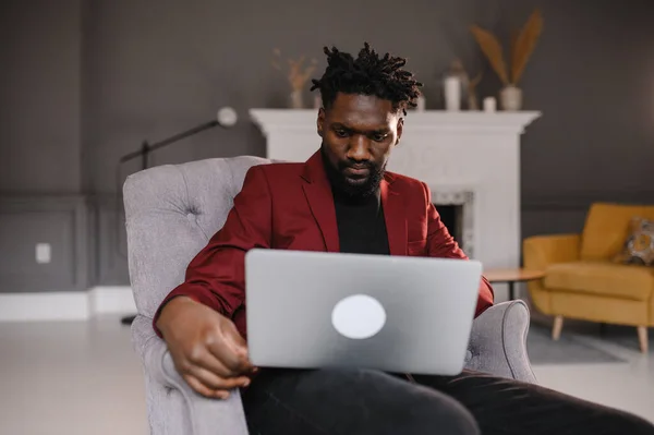 Sorrindo milenar homem casual afro-americano trabalhando com aplicativos ou se comunicando on-line no laptop — Fotografia de Stock