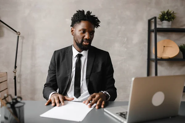 Vista frontal tiro na cabeça jovem sorridente empresário afro-americano olhando para a tela do laptop, lendo mensagens agradáveis em redes sociais, trabalhando no computador sentado à mesa em casa de escritório. — Fotografia de Stock