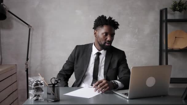 穿着经典西装的英俊的非洲商人在办公室工作时使用笔记本电脑，微笑着 — 图库视频影像