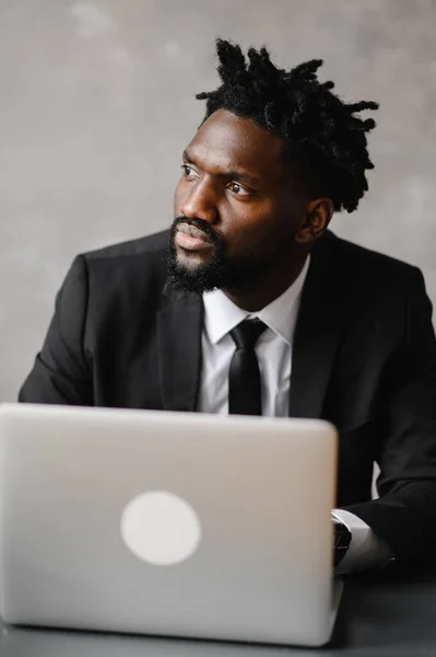 Homem de negócios um homem afro-americano de terno trabalha em um laptop em seu escritório moderno — Fotografia de Stock