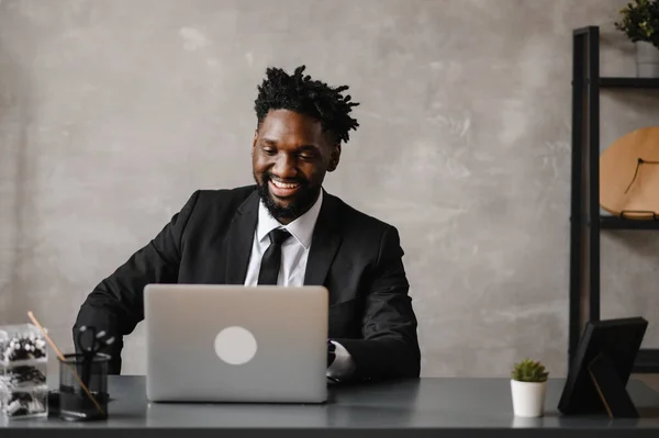 Homem de negócios um homem afro-americano de terno trabalha em um laptop em seu escritório moderno — Fotografia de Stock