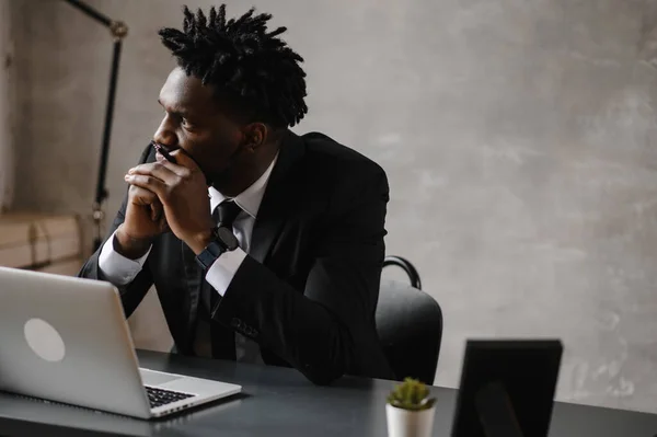 Homem de negócios um homem afro-americano de terno trabalha em um laptop em seu escritório moderno — Fotografia de Stock