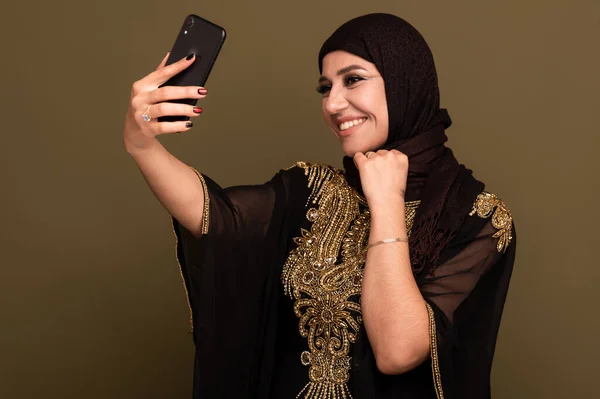 Donna musulmana che ride tenendo lo smartphone in mano e scattando selfie — Foto Stock