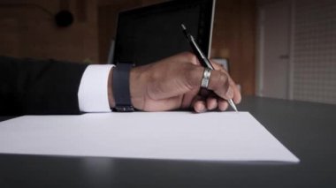Takım elbiseli siyah bir işadamı bir kağıt parçasına notlar alır. Bir bilgisayarla uzaktan öğrenme