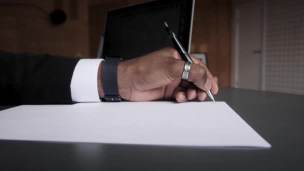 Un hombre de negocios negro con traje toma notas en una hoja de papel. Aprendizaje electrónico de forma remota a través de un ordenador — Vídeos de Stock