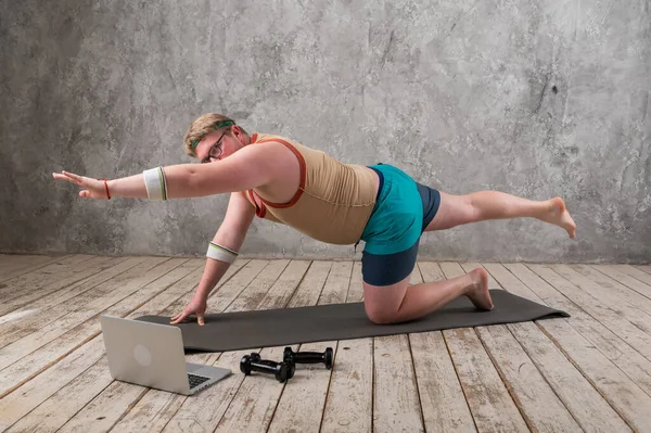 Pria gemuk yang lucu dalam pakaian olahraga melakukan latihan melihat ke dalam laptop. latihan di rumah — Stok Foto