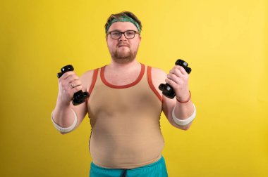 komik şişman adam dambıllarla egzersiz yapıyor. Fazla kilolu. sarı arkaplan