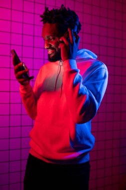 Müzik konsepti. Zenci bir adam kulaklıkla neon ışığın arka planında müzik dinler. Kırmızı ve mavi arkaplan