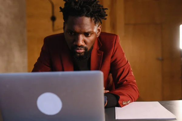 Um negro focado num fato está a trabalhar num portátil. Trabalho remoto em casa — Fotografia de Stock