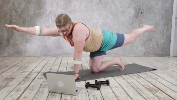 Overgewicht man oefenen, doen stretching oefeningen op yoga mat, kijken fitness video 's online op laptop thuis. yoga oefeningen online met laptop — Stockvideo