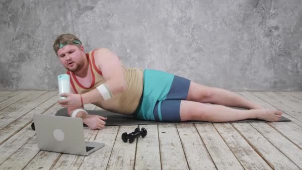 Hombre gordo divertido haciendo deportes en la estera de yoga, haciendo deportes en línea, mirando en el ordenador portátil — Vídeos de Stock