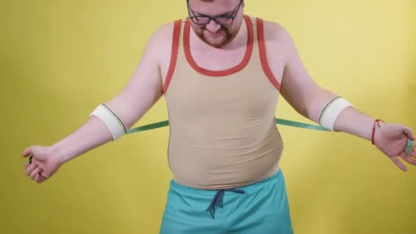 Смешной толстяк в спортивной одежде измеряет объем тела — стоковое видео