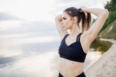 Kolsuz tişörtlü atletik kız plajda esneme hareketleri yapıyor.