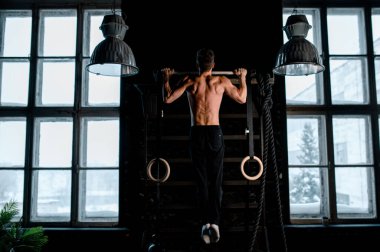 Sporcu kaslı erkek model spor salonunda yatay çubuğa yanaşıyor.