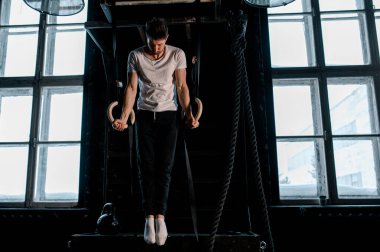 Spor salonunda jimnastik yüzükleri olan genç bir erkek atlet. Yüzüklere odaklan