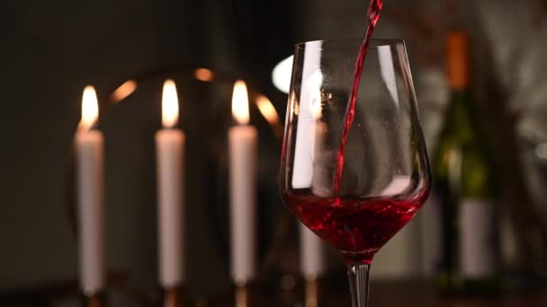 Rode wijn wordt uit een fles in een doorzichtig glas gegoten. romantisch diner bij kaarslicht met een glas wijn — Stockvideo