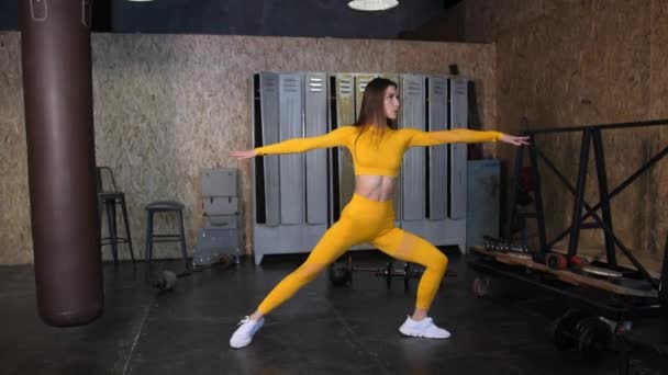 Een mooi meisje in een geel trainingspak doet stretching. Moderne sporthal met grote ramen — Stockvideo