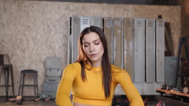 Une belle fille en survêtement jaune fait des étirements. Salle de sport moderne avec de grandes fenêtres — Video