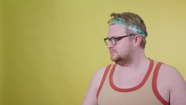 Funny fat man in sportswear with dumbbells in his hands. Overweight man goes in for sports. Yellow background isolate — Stock Video