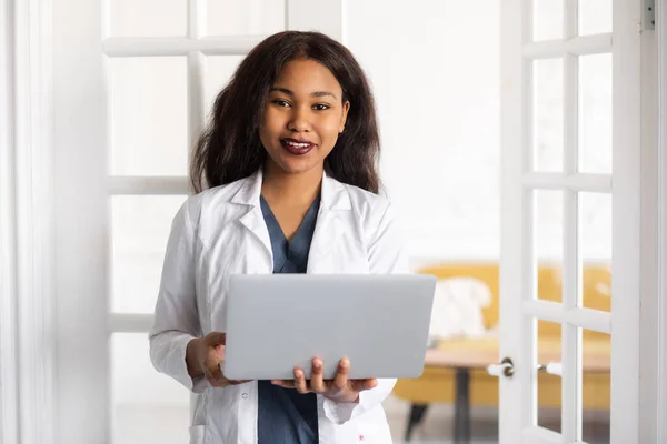 black skinned female medic smiling standing on a white background with papers in hand