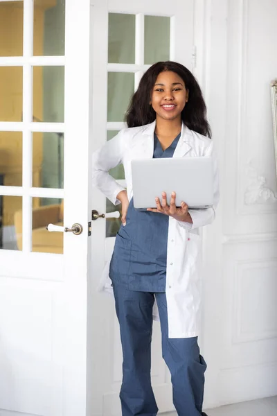 black skinned female medic smiling standing on a white background with papers in hand